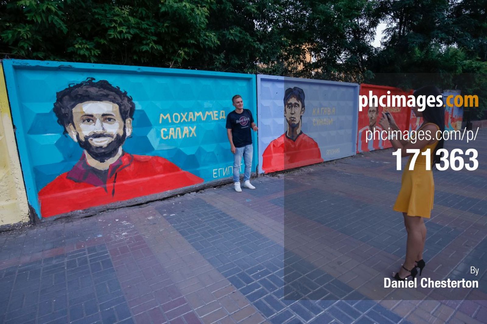 Fans pose in front of a mural of Mohamed Salah