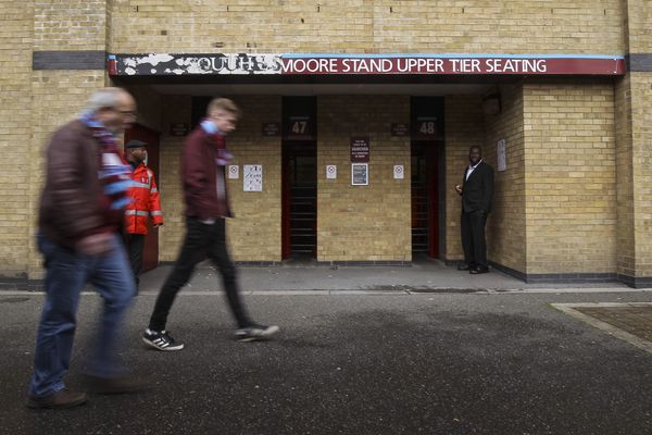 Fans walk past the Bobby Moore stand with old signage for the South Stand showing