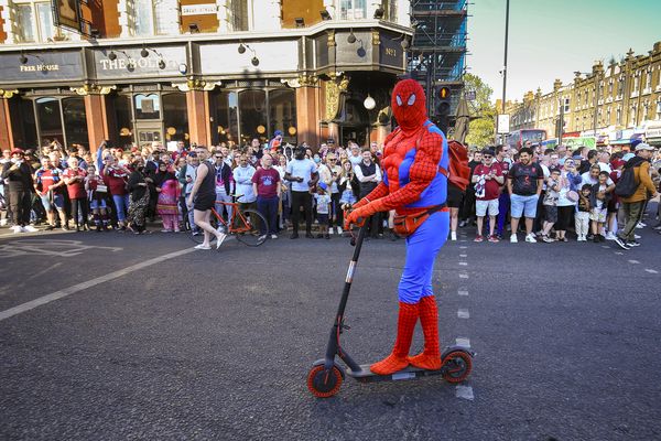 A man dressed as spiderman on a scooter drives past crowds waiting for the parade